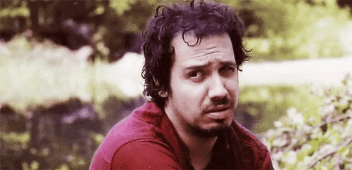 a man with curly hair and a beard is sitting in front of a pond .