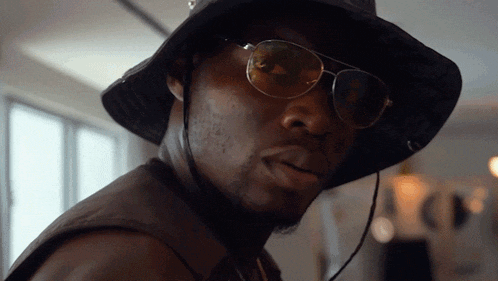 a man wearing a hat and sunglasses looks to the side