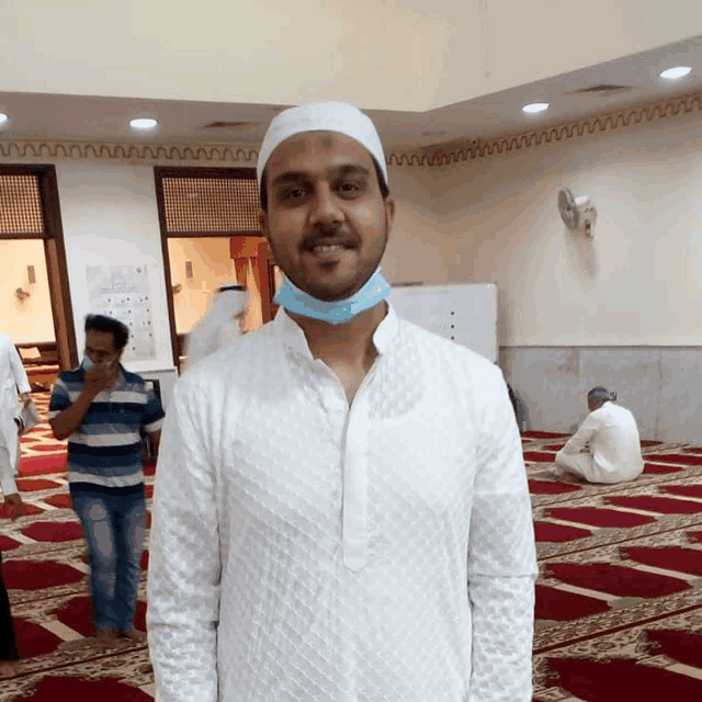 a man wearing a white shirt and a blue mask smiles in a mosque