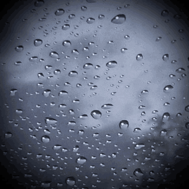 rain drops on a window with a cloudy sky behind them