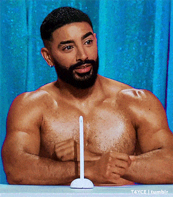 a shirtless man with a beard is sitting at a table with a stick in his chest .