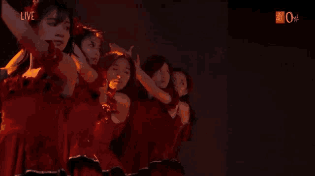 a group of women in red dresses are dancing in front of a screen that says " live "