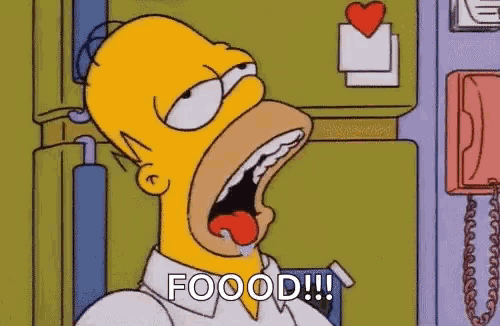 homer simpson is sitting in front of a refrigerator with his mouth open and his tongue out .