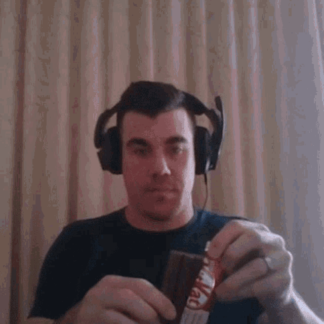 a man wearing headphones is holding a kitkat bar in his hand .