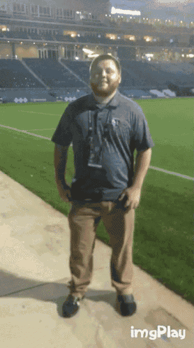 a man is standing on a sidewalk in front of a stadium with imgplay written in the corner