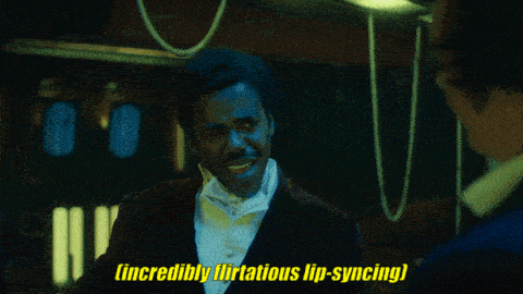 a man says " incredibly flirtatious lip-syncing " in a dark room