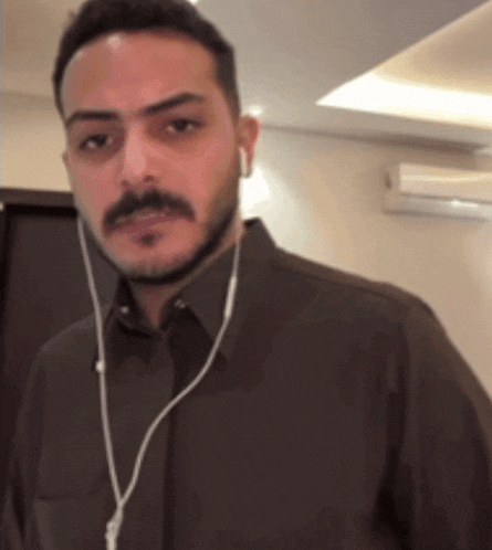 a man with a beard wearing ear buds and a brown shirt