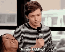 a man in a striped shirt is holding a microphone and talking to a woman who is laughing .