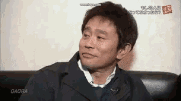 a man in a suit is sitting on a couch and making a face .