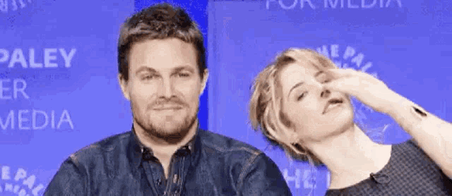 a man and a woman are posing for a picture in front of a blue wall that says paley