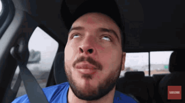 a man with a beard is sitting in a car with a subscribe button