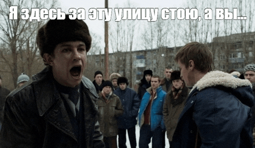 a man in a fur hat is yelling at another man in front of a crowd with russian writing on the bottom