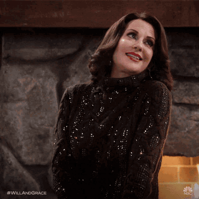 a woman in a sequined sweater stands in front of a fireplace