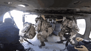 a group of soldiers are kneeling down in a helicopter while a man holds a video game controller
