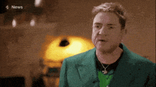 a man in a green suit and necklace is talking on a tv show .
