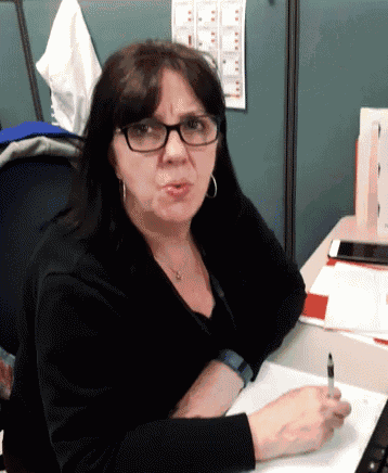 a woman wearing glasses sits at a desk with a pen