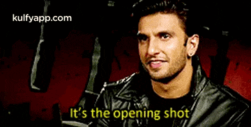 a man in a leather jacket is smiling and saying `` it 's the opening shot ''