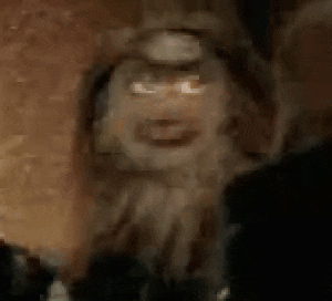 a close up of a monkey 's face with a beard and teeth in a dark room .