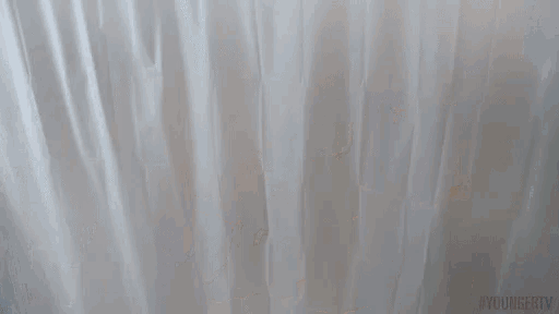 a woman is holding a white shower curtain in her hands .