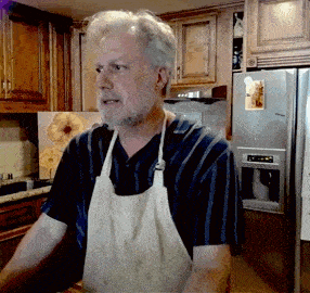a man wearing an apron is standing in front of a stainless steel refrigerator