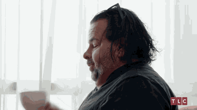 a man with long hair and a beard is sitting in front of a window with tlc written on the bottom