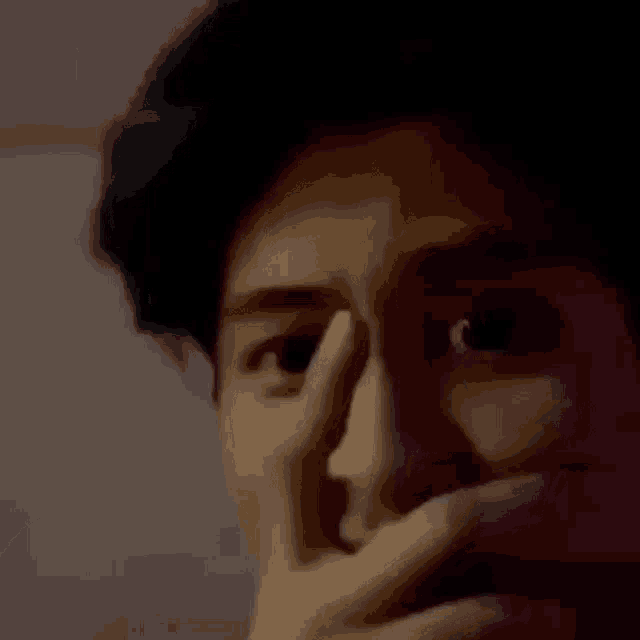 a man is covering his mouth with his hand and looking at the camera .