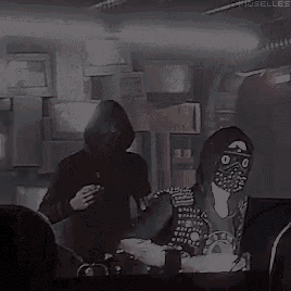 a couple of people are standing next to each other in a dark room . one of the people is wearing a mask .