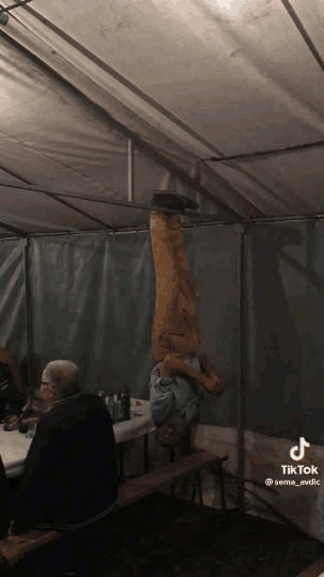 a man is doing a handstand upside down in a tent while sitting at a table .