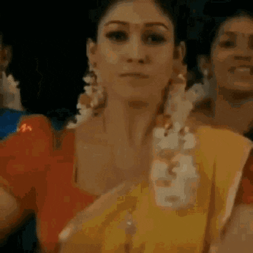 a woman in a yellow saree and a red top is standing in front of a crowd of people .