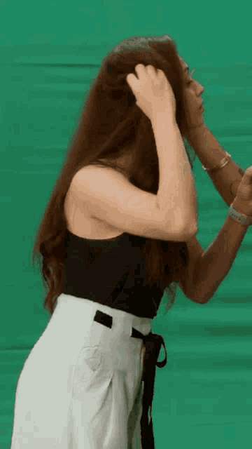 a woman in a black tank top and white pants is standing in front of a green screen