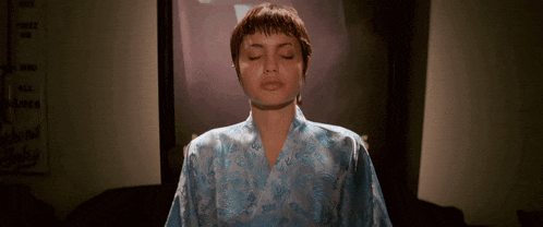 a woman in a blue robe is meditating with her eyes closed in front of a tv screen