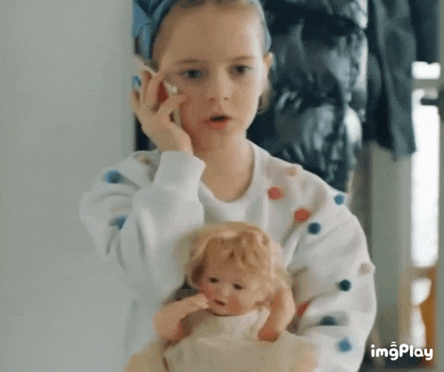 a little girl is holding a doll and talking on a phone .