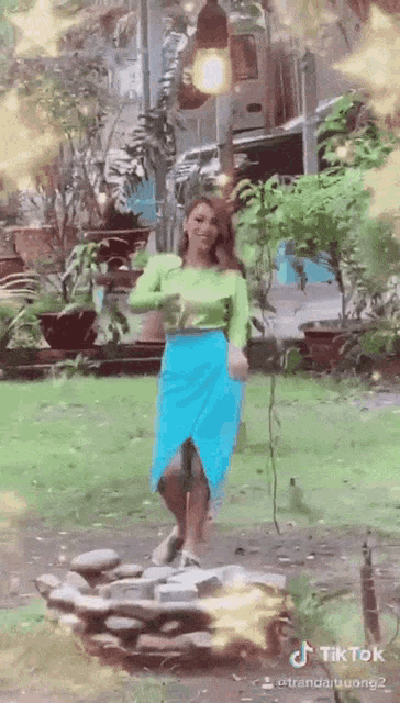 a woman in a green top and blue skirt is dancing in a park .