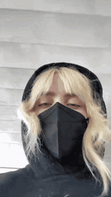 a woman with blonde hair wearing a black mask and a black hoodie