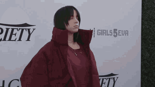 a woman in a red jacket is standing in front of a white wall .