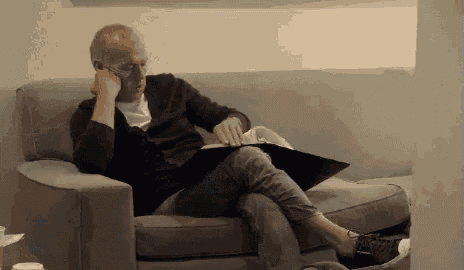a man is sitting on a couch talking on a cell phone and reading a book .