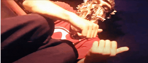 a man wearing a red shirt with a white circle on it is making a hand gesture
