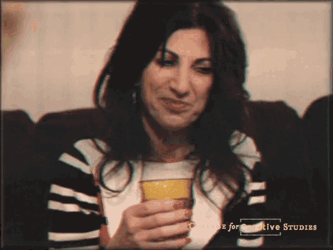 a woman sitting on a couch holding a yellow cup with college for creative studies written on it