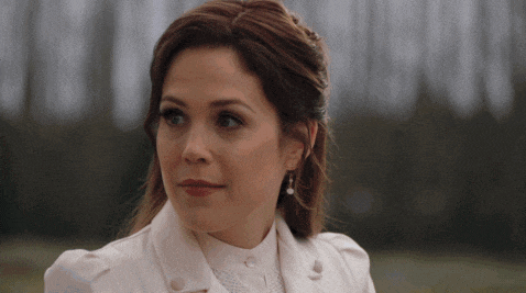 a woman in a white coat and pearl earrings looks at the camera