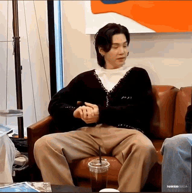 a man is sitting on a couch with his legs crossed and a cup of coffee in front of him .