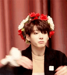 a young man wearing a flower crown on his head is holding a white object .