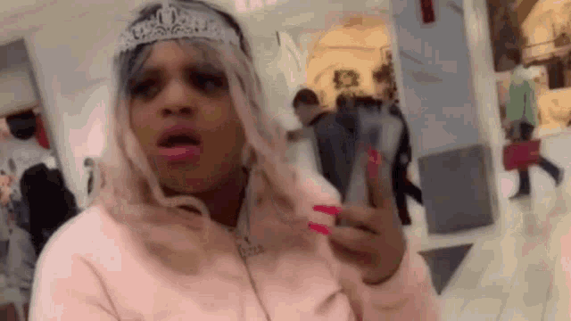 a woman wearing a tiara and pink lipstick is making a funny face in a shopping mall .