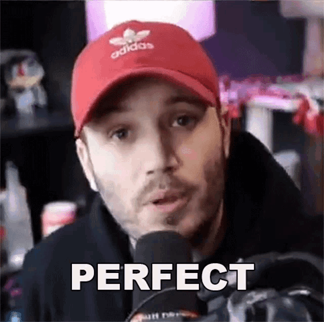 a man wearing a red adidas hat is talking into a microphone and saying perfect