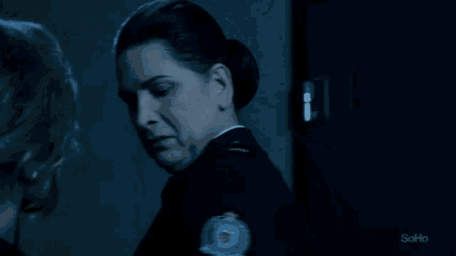 a woman in a police uniform talks to another woman in a dark room with soho written on the bottom of the screen