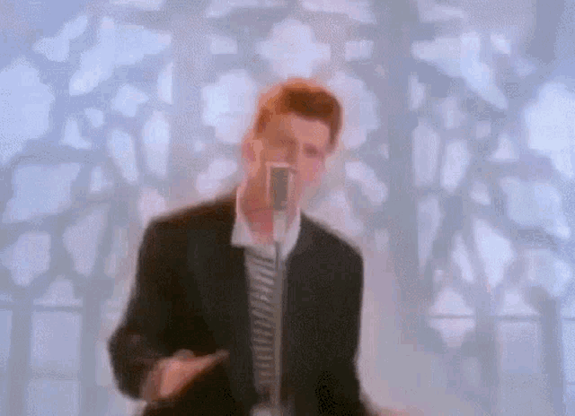 a man in a suit is singing into a microphone in front of a stained glass window .