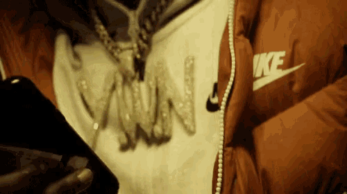 a person wearing a nike jacket and a necklace with the letter w on it