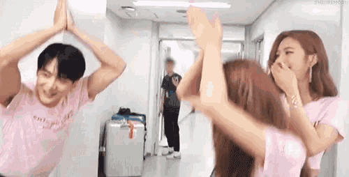 a man and two women are standing next to each other in a hallway with their hands in the air .