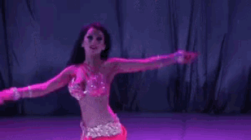 a belly dancer is dancing in front of a purple curtain on a stage .