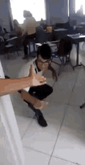 a man is kneeling on the floor in a classroom while a person holds his leg .