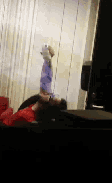a man in a red shirt is laying on a couch holding a bottle of water